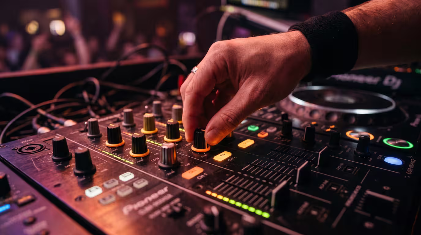 A hand turning the low-frequency EQ knob on a club DJ mixer channel strip