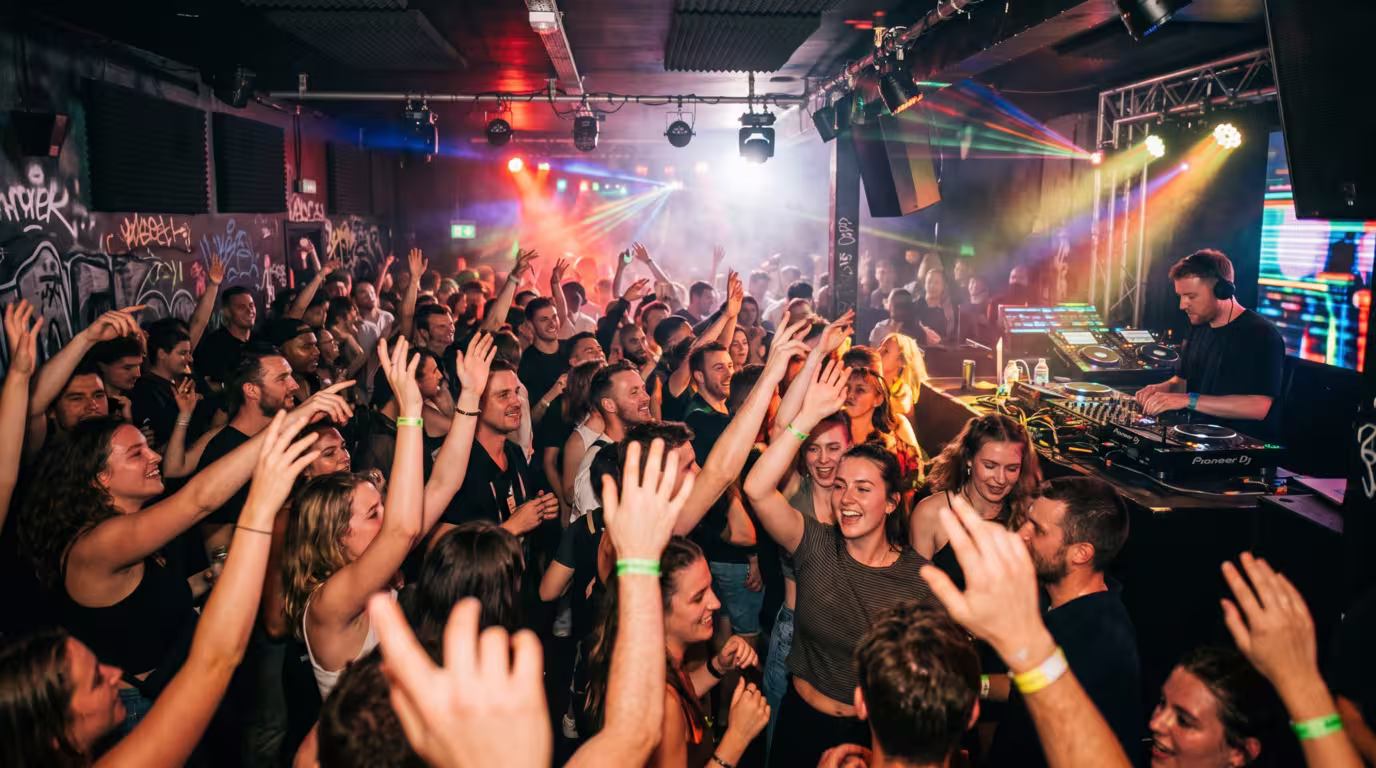 A busy club night with a happy crowd dancing in front of a DJ