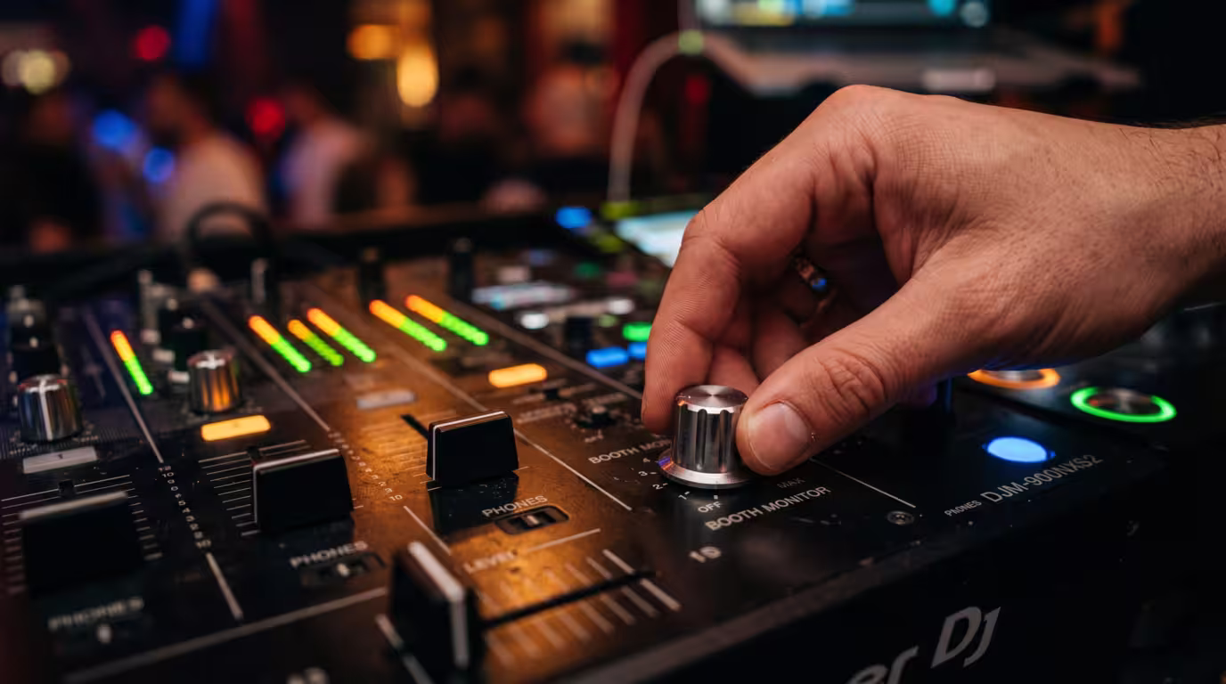 A DJ's hand on the booth monitor level knob of a club mixer